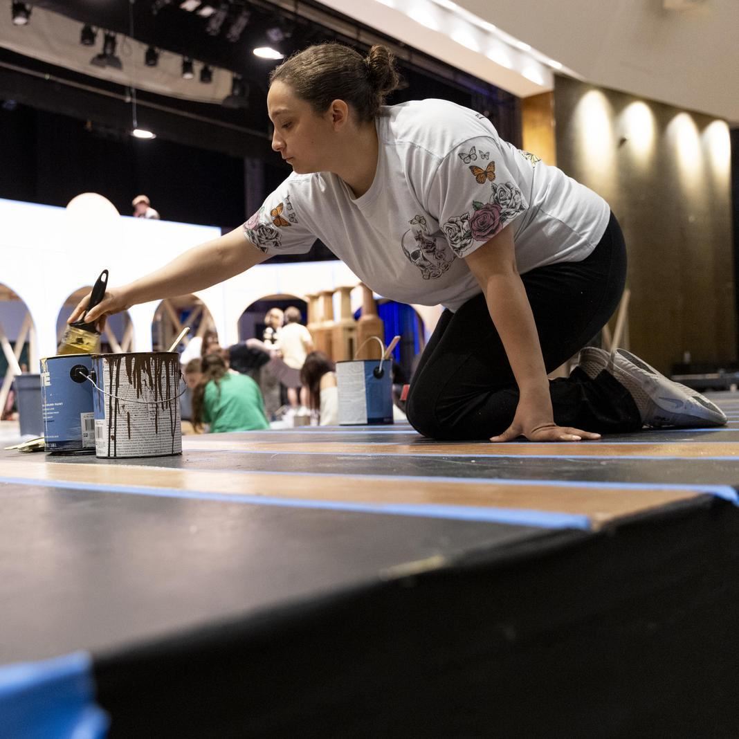  A student on her knees paints a stage set